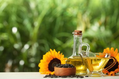 Ayçiçeği pişirme yağı, tohumlar ve sarı çiçekler beyaz ahşap masa üzerinde açık havada, metin için boşluk