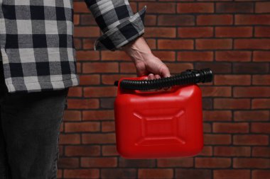 Man holding red canister against brick wall, closeup
