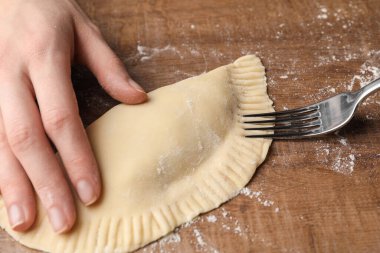 Woman making chebureki at wooden table, closeup
