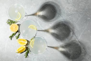 Martini glasses of refreshing cocktail decorated with lemon slices and rosemary on light grey textured table, flat lay. Space for text