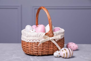 Easter basket with many painted eggs on grey textured table