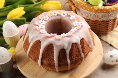 Delicious Easter cake decorated with sprinkles near painted eggs and tulips on wooden table, closeup