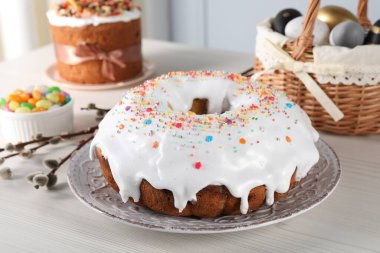 Delicious Easter cake decorated with sprinkles near willow branches, candies and painted eggs on white wooden table