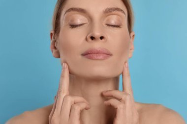 Woman massaging her face on turquoise background