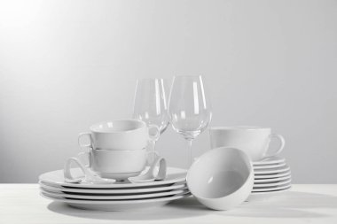Set of clean dishware and glasses on white wooden table against light background