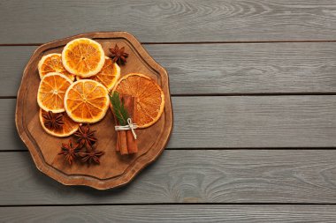 Flat lay composition with dry orange slices, anise stars and cinnamon sticks on grey wooden table. Space for text