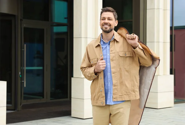 Attractive happy man holding garment cover with clothes outdoors. Dry cleaning service