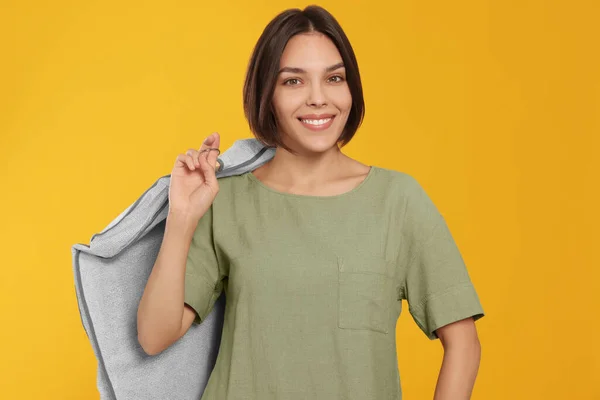 Woman holding garment cover with clothes on yellow background. Dry-cleaning service
