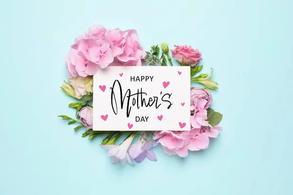 Happy Mother\'s Day greeting card and beautiful flowers on pale light blue background, flat lay