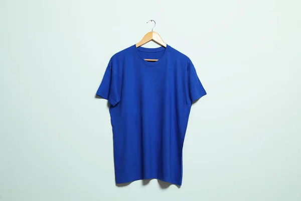 Hanger with blue t-shirt on light wall. Mockup for design