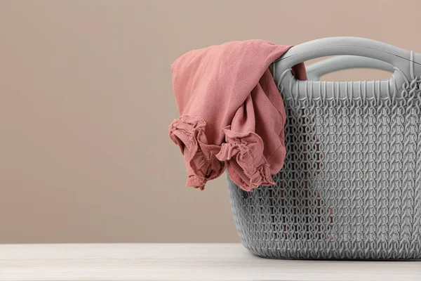 Plastic laundry basket with clothes near beige wall. Space for text