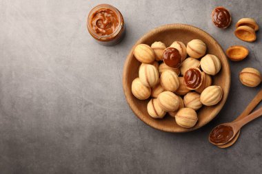 Delicious nut shaped cookies with boiled condensed milk on gray textured table, flat lay. Space for text