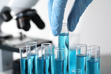 Scientist taking test tube with light blue liquid in laboratory, closeup