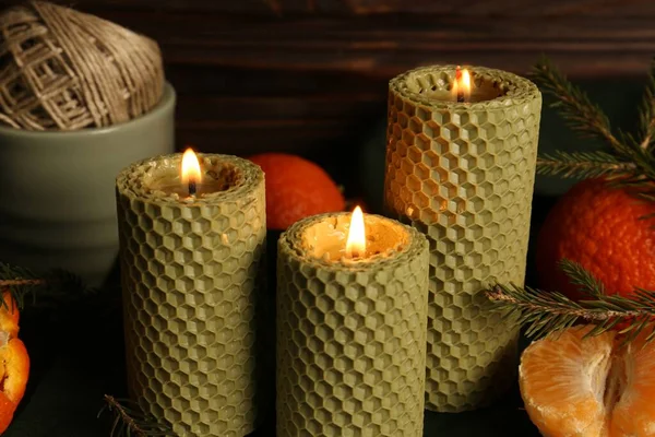 Beautiful burning beeswax candles, spruce twigs and tangerines on table, closeup