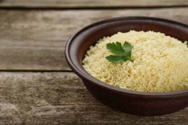 Tasty couscous with parsley on wooden table, closeup. Space for text