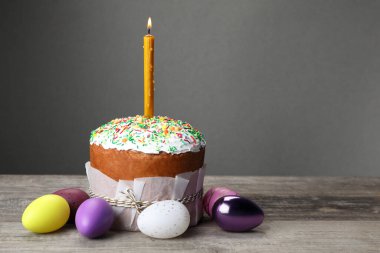 Traditional Easter cake with sprinkles, burning candle and painted eggs on wooden table, space for text