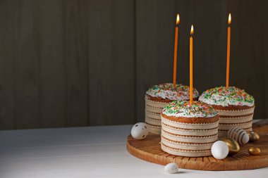 Traditional Easter cakes with sprinkles, candles and decorated eggs on white table. Space for text