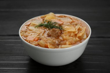 Tasty cabbage soup with meat, carrot and dill on black wooden table, closeup