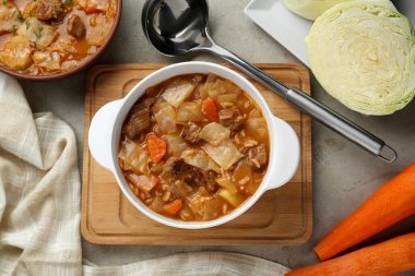 Tasty cabbage soup and ingredients on light grey textured table, flat lay