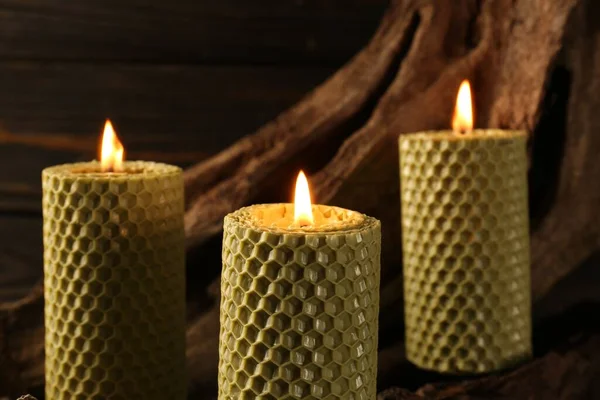 Beautiful burning beeswax candles on snag, closeup