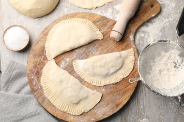 Raw chebureki with tasty filling and rolling pin on wooden table, flat lay