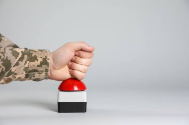 Serviceman pressing red button of nuclear weapon on light gray background, closeup with space for text. War concept