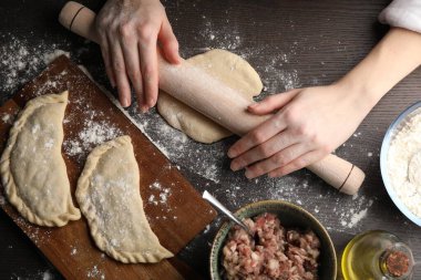 Woman rolling dough for chebureki at wooden table, top view