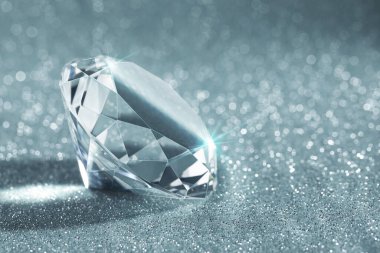 Beautiful shiny diamond on glitter background, closeup. Space for text