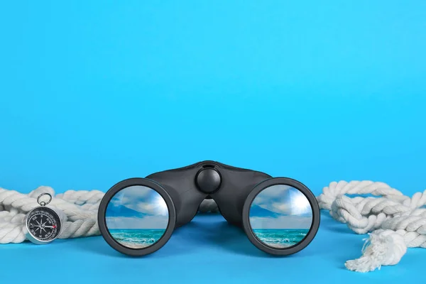 Binoculars, compass and rope on light blue background. Seascape reflecting in lenses