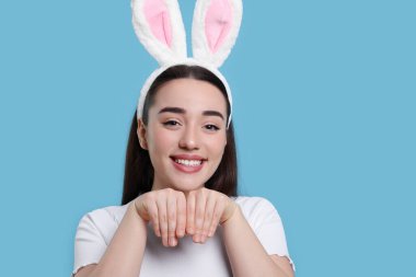 Happy woman wearing bunny ears headband on turquoise background, space for text. Easter celebration