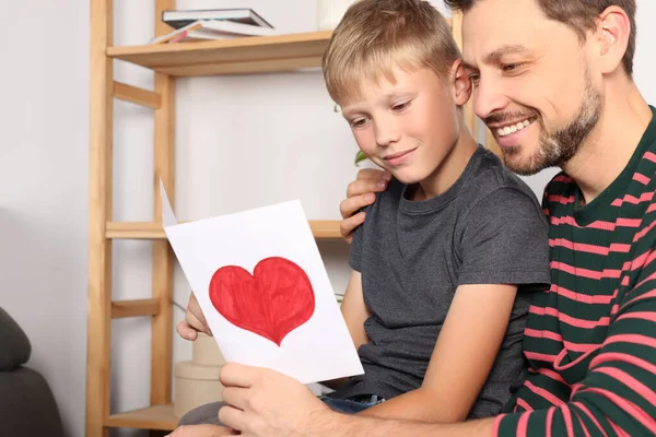 Happy man receiving greeting card from his son at home