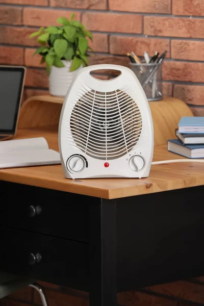 Modern electric fan heater near notebooks on wooden table in office