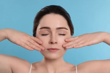 Young woman massaging her face on turquoise background