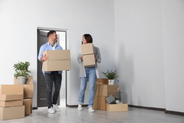 Happy couple with moving boxes entering in new apartment