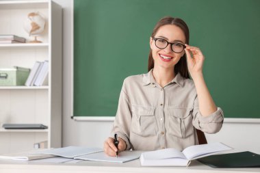 Portrait of beautiful young teacher at table in classroom