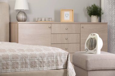 Modern electric fan heater on pouf in cozy room