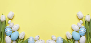 Flat lay composition with decorated Easter eggs and flowers on pale yellow background, space for text. Banner design