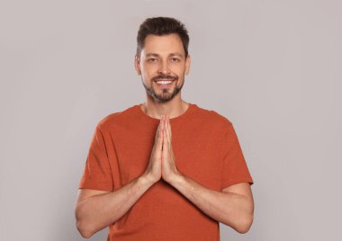 Elleri sıkıca bağlı açık gri arka planda dua eden adam.