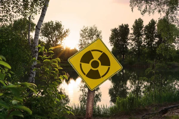 Radioactive pollution. Yellow warning sign with hazard symbol near contaminated area outdoors