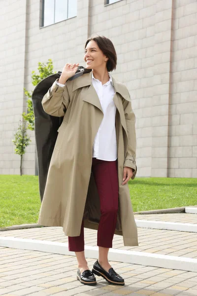 Woman holding garment cover with clothes outdoors. Dry-cleaning service