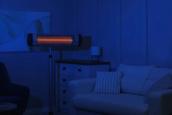 Electric infrared heater in dark living room at night