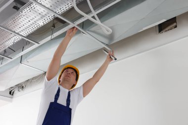 Worker installing metal frame indoors. Suspended ceiling