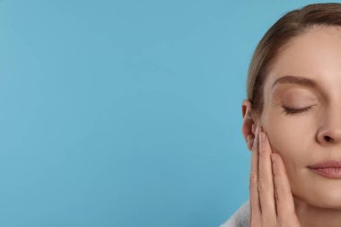 Woman massaging her face on turquoise background, closeup. Space for text