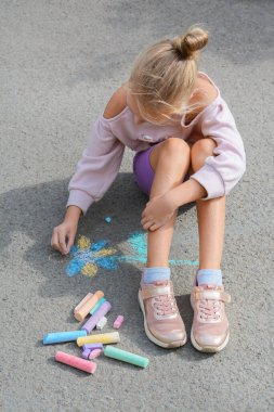 Little child drawing flower with chalk on asphalt