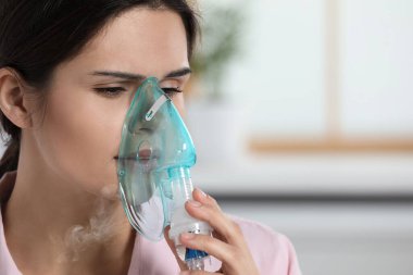 Sick young woman using nebulizer at home, closeup. Space for text