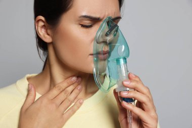 Sick young woman using nebulizer on grey background, closeup. Space for text