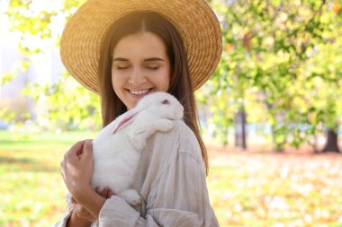 Happy woman holding cute white rabbit in park