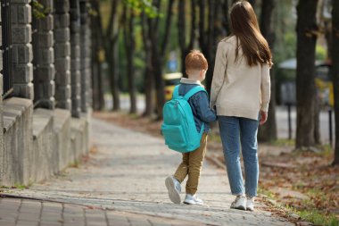 Young mom taking her son to school, back view