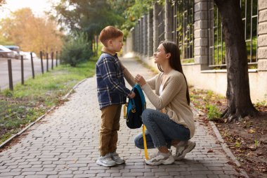 Young mom giving school backpack to her son outdoors