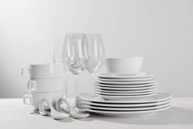 Set of clean dishware and glasses on white wooden table against light background